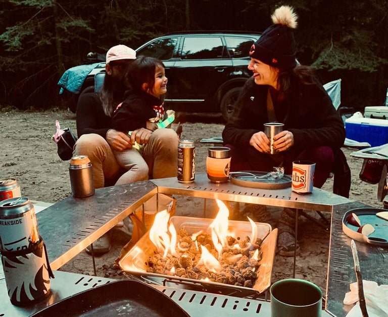 Family smiling and relaxing around a Campingmoon MT-045 fire pit powered by the Zutto SP1 smokeless propane gas adapter surrounded by a Snow Peak Jikaro Fire Ring table